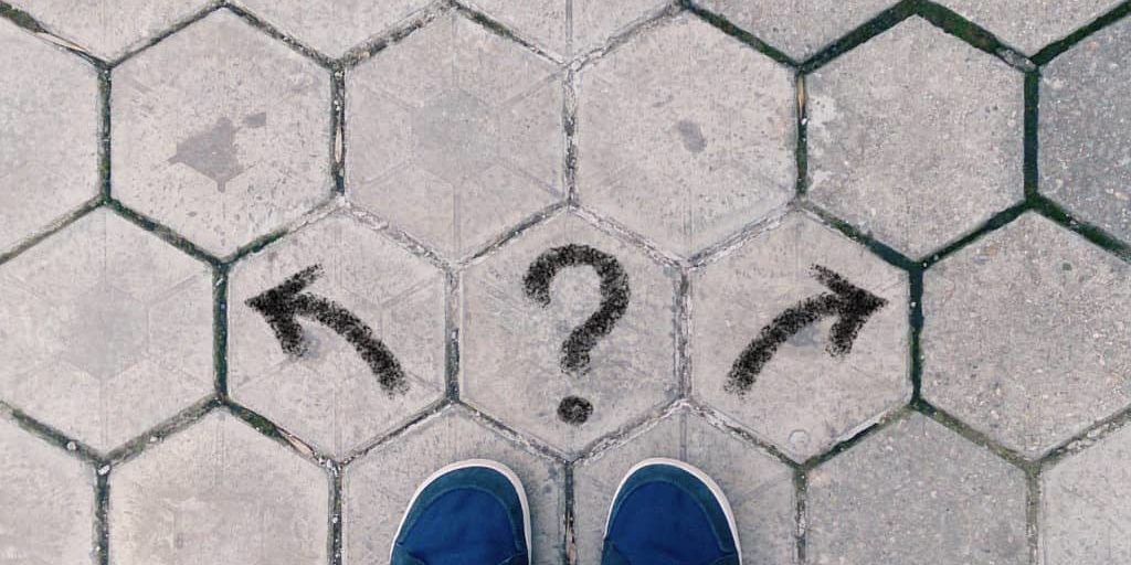 Top view of blue shoes on tiled pavement with questionmark and t Top view of blue shoes on tiled pavement with questionmark and two arrows, concept of crossroads, taking decisions and choosing the right way